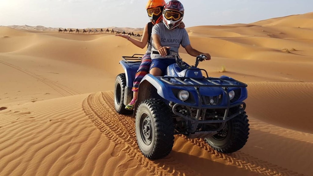 Quad biking tour couple on a Quad Bike with Camels in the Background.